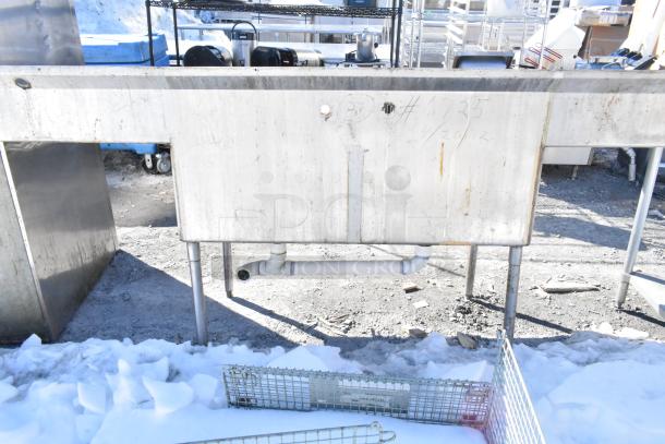 Commercial 2 bay sink with dual drain boards, stainless steel, lightly worn, visible pipe fittings, suitable for kitchens.