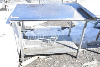 Commercial table with metal top and undershelf, sturdy metal legs, slight wear, wire basket included, ideal for kitchen use.