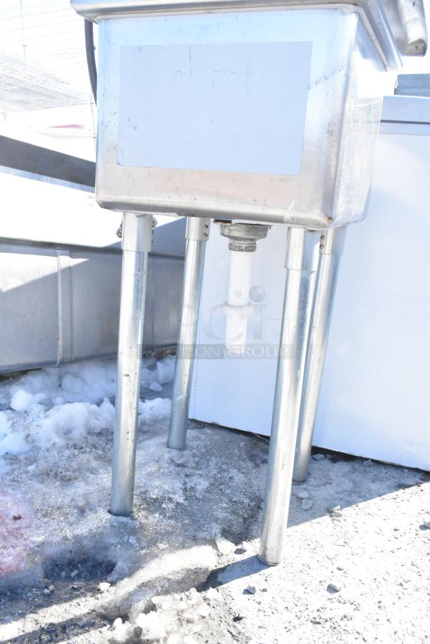 Commercial single bay sink with faucet and handles, stainless steel, mounted on four legs, visible plumbing connections.