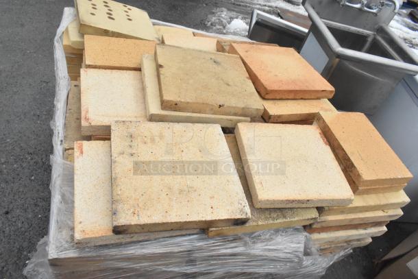 200 pizza oven cooking stones stacked on a pallet, various shades of beige and tan, suitable for high-heat baking.