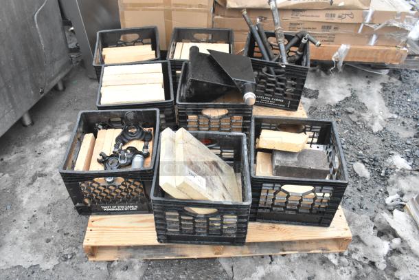 Pallet lot with various items, including cooking stones for pizza oven and black metal legs, in milk crates on wooden pallet.