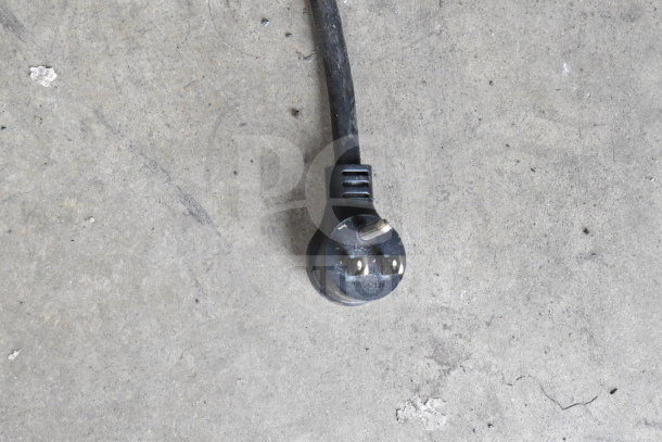 Close-up of a black power plug on a concrete surface, part of a 2018 True GDM-12-HC cooler merchandiser.