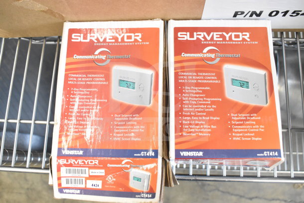 Two new Surveyor CT414 commercial thermostats in boxes, featuring 7-day programmability, dual setpoint, and Internet control.