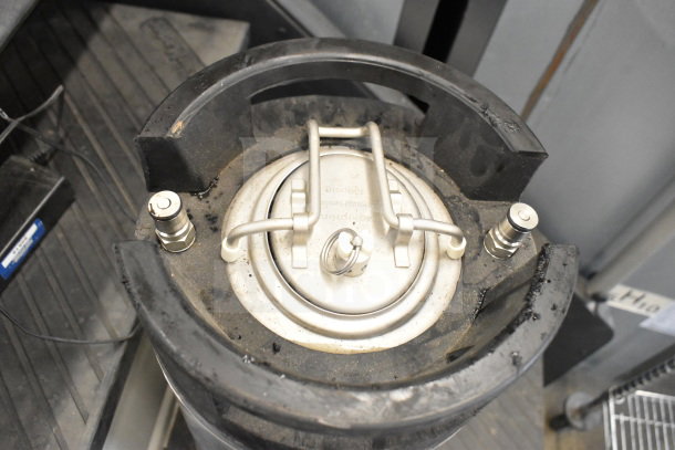 Stainless steel keg, model K1109(2), with a secure lid and valve fittings, showing moderate wear and some dust accumulation.