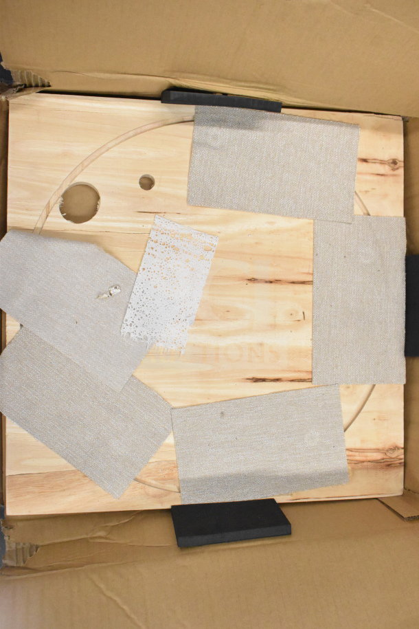 Three boxes containing a wooden board with cutouts, covered with textured fabric patches, shown in a cardboard box.