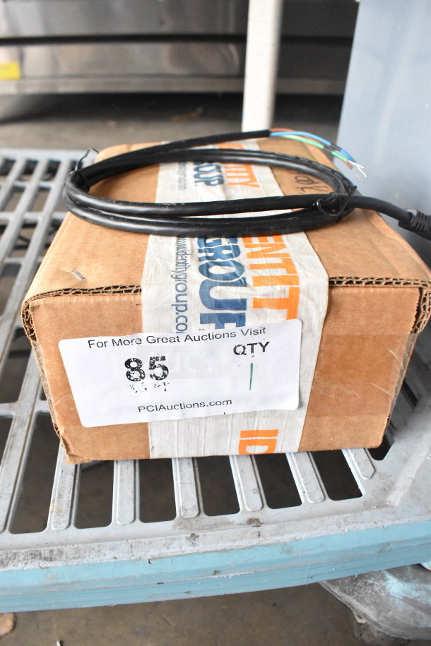 Cardboard box labeled "Identity Group" with auction sticker showing "85 QTY 1." Box is sealed and adorned with a coiled black cable.