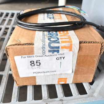 Cardboard box labeled "Identity Group" with auction sticker showing "85 QTY 1." Box is sealed and adorned with a coiled black cable.
