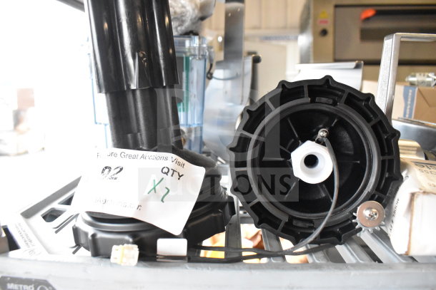 2 black units with gear-like features, labeled "Qty x2." Appears unused on a metal shelf, includes a cable and tags.