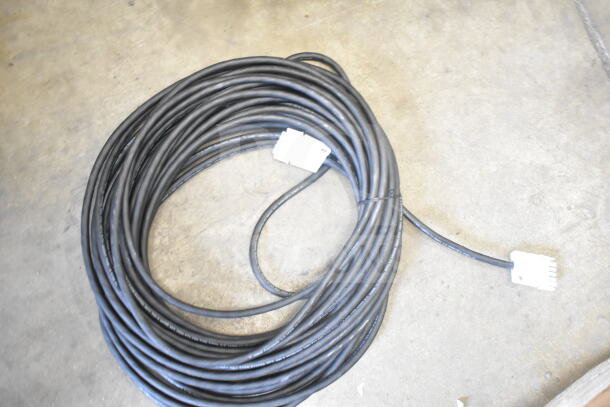 Coiled black cable with white connectors on a concrete floor; part of an auction item: Box w/ Insulation Strip, Hose, Cable.