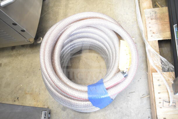 Coiled heavy-duty hose with a protective mesh cover on a wooden pallet, featuring an attached yellow label and blue tape.
