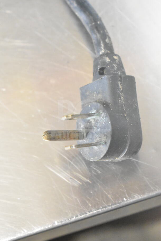 The image shows an electrical plug with a three-prong connector, indicating it requires a 115-volt outlet. The plug has some visible wear and tear.