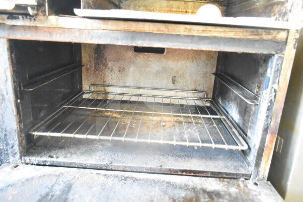 American Range commercial gas 6-burner range oven interior, showing wear and usage marks, with metal rack in place.