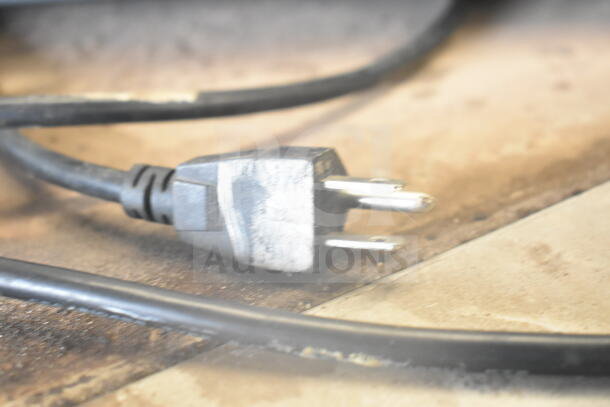 Close-up of a power plug with a black cord, part of an Open Light Up Sign; details of sign not visible.