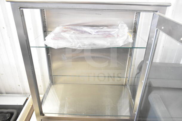 Shampaine Commercial Merchandising Cabinet with glass shelves, stainless steel frame, and clear visibility, in used condition.