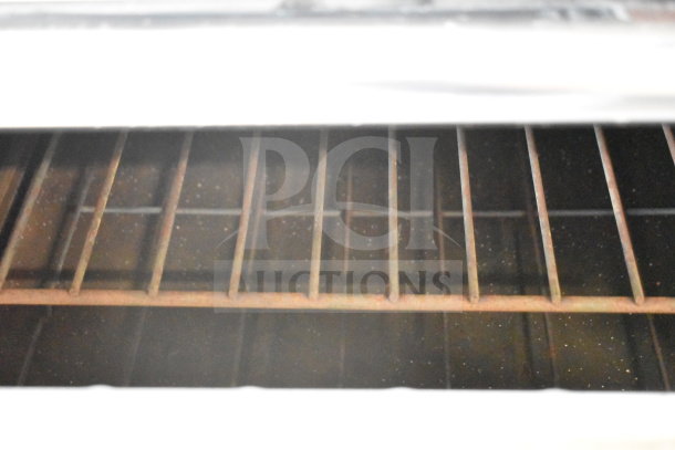 Interior view of Garland commercial oven, showing metal racks, part of a flat top griddle with 2 burners. Signs of wear visible.
