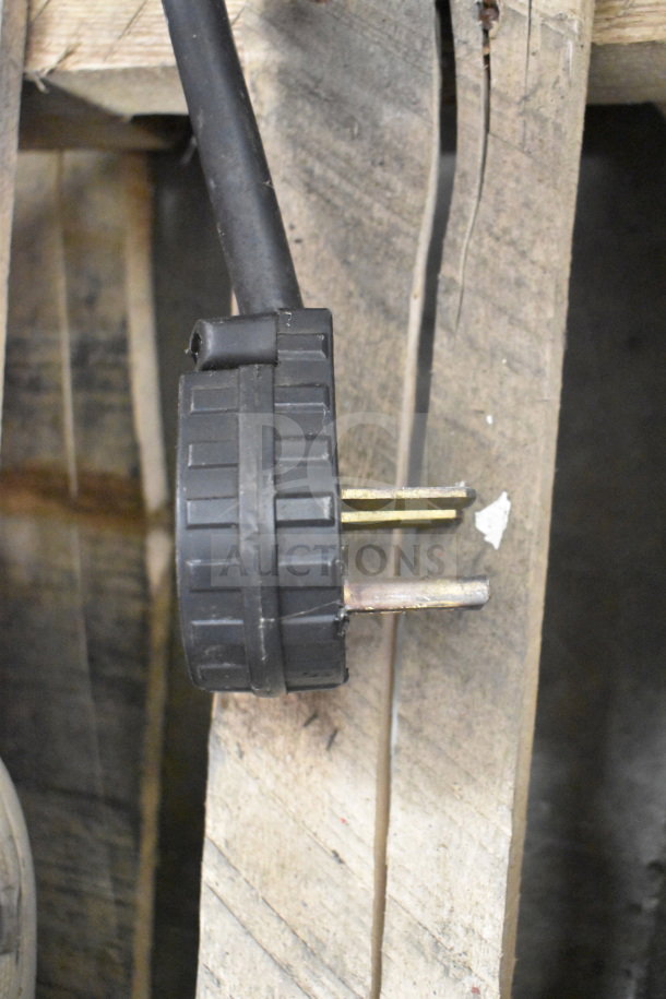 Power plug of a Cooking Performance Group convection oven, showing a three-pronged plug positioned against a wooden surface.