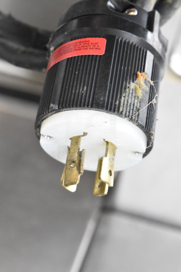 Close-up of the plug of a Hobart 6614 commercial meat saw, showing electrical prongs and a red warning label.