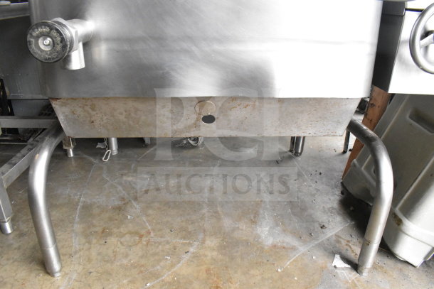 Commercial floor-style manual tilt braising pan with stainless steel finish. Visible signs of use and corrosion on the surface.