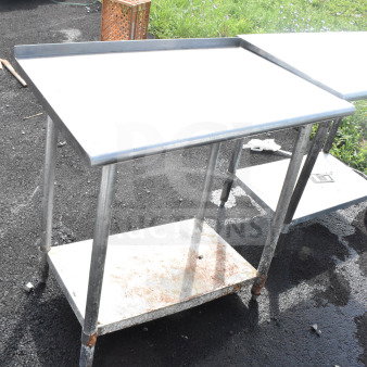 Commercial metal table with under shelf, showing signs of rust and outdoor wear, ideal for heavy-duty use.