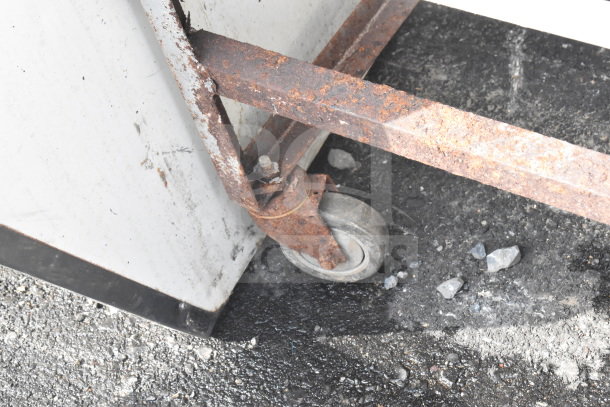 Rusty commercial pan transport rack with industrial caster. Visible wear indicates need for maintenance.