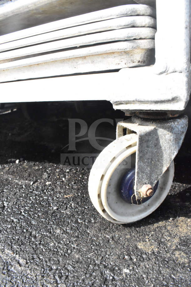 Commercial pan transport rack with durable casters, featuring 50 baking pans. Visible wear on casters; ideal for bakery use.