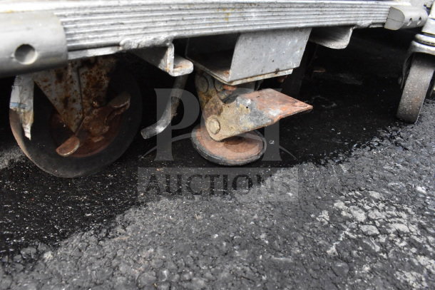 Commercial pan transport rack with industrial casters, shown with 36 baking pans. Visible rust on casters indicates wear.
