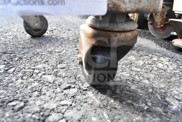 Commercial Bowl Dolly with rusted commercial caster on asphalt, showing wear. Suitable for moving heavy bowls.