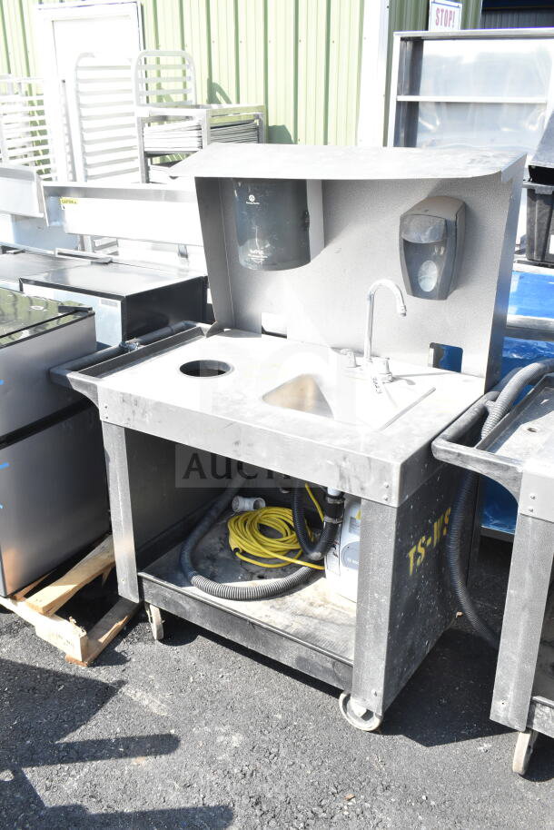Commercial portable sink on casters, features a basin, faucet, waste storage, and dispensers. Visible wear on surface.