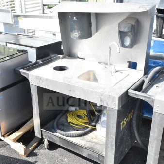 Commercial portable sink on casters, features a basin, faucet, waste storage, and dispensers. Visible wear on surface.