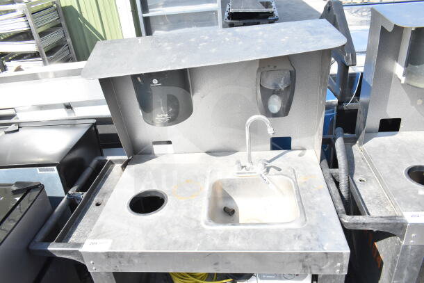 Commercial portable sink on casters, equipped with faucet, built-in soap and towel dispensers, stainless steel surface in fair condition.