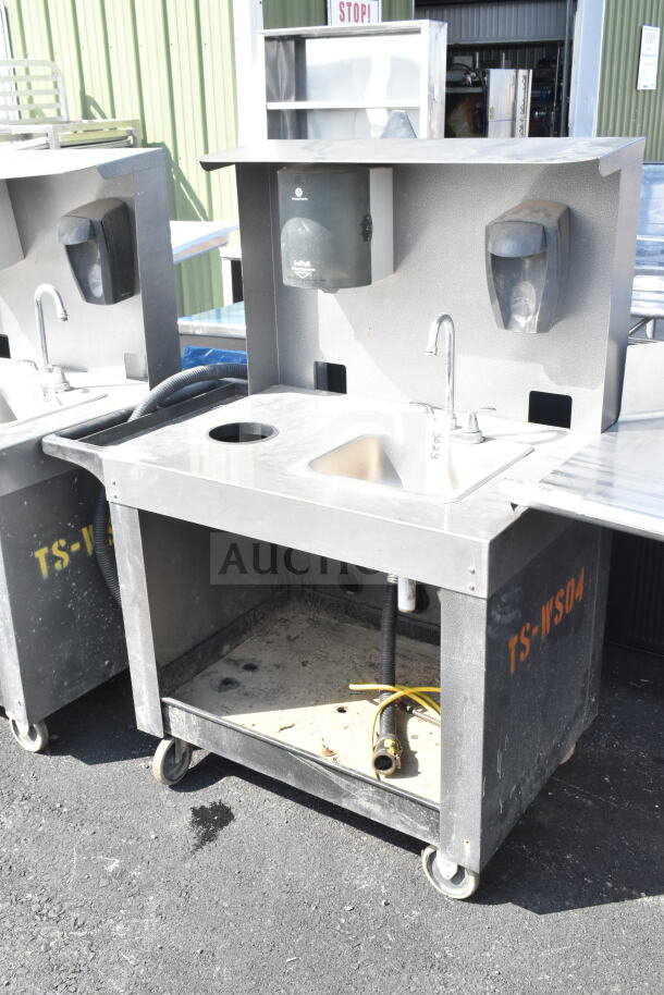 Commercial portable sink on casters, gray-black color with integrated soap dispensers, faucet, and storage space.