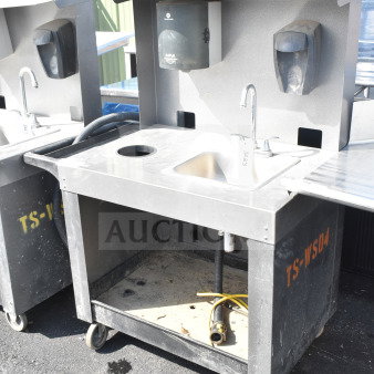 Commercial portable sink on casters, gray-black color with integrated soap dispensers, faucet, and storage space.