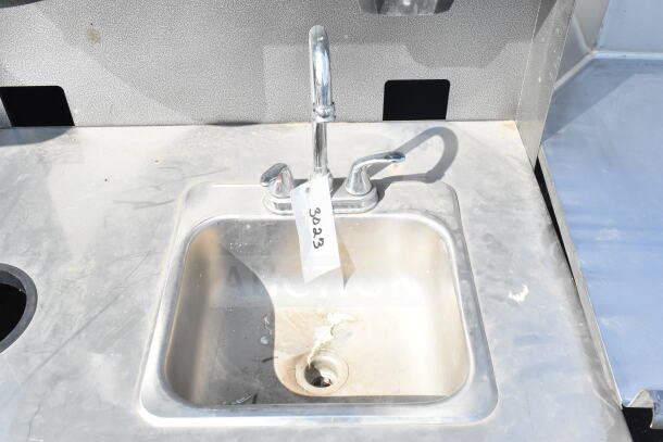 Commercial portable sink with faucet, stainless steel, tag labeled "3023," on commercial casters, moderate wear.