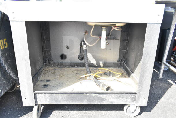 Commercial portable sink with under-sink plumbing and visible dirt, mounted on sturdy commercial casters for mobility.
