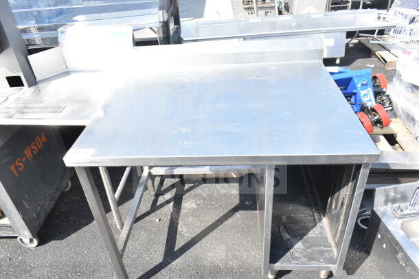 Stainless steel commercial table with backsplash, open lower shelf, sturdy legs, minimal wear. Ideal for kitchen use.