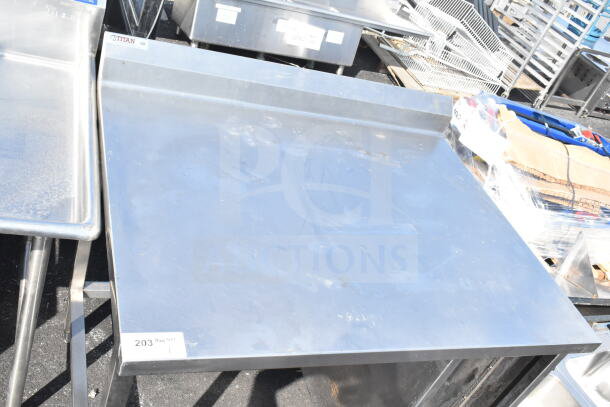 Stainless steel commercial table with raised edges, Titan brand label, sturdy legs, and minor surface scratches.