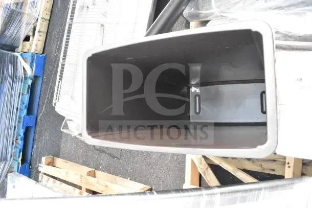 Brand new scratch and dent utility sink, black finish, surrounded by pallets and wrapped items. Close-up view.
