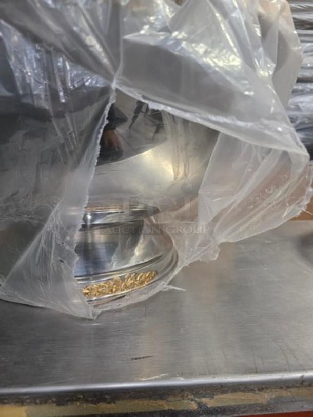 Stainless steel punch bowl partially wrapped in plastic, featuring a decorative base with gold accents.