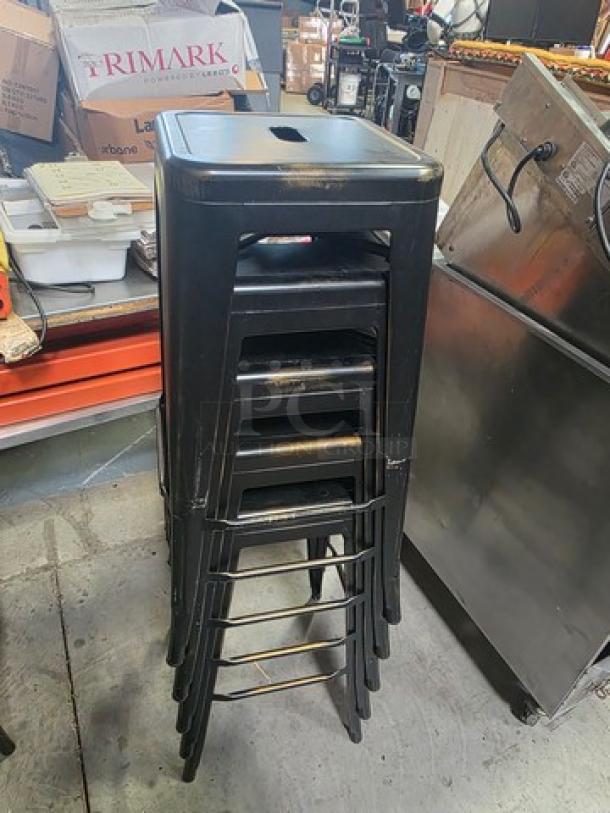 Lot of 6 black metal bar stools, stackable design. Used condition, surface wear visible. Ideal for high-traffic areas.