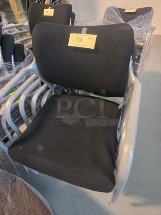 Lot of 5 stacking chairs with black fabric seats and gray powder-coated frames. Visible wear on seats. Quantity label marked "73".