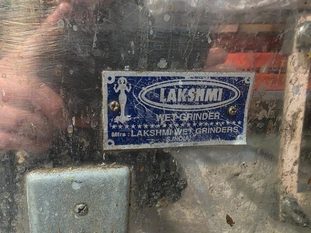 Lakshmi Tilting Commercial Wet Grinder with visible wear. Features metal body with blue manufacturer label indicating "Lakshmi Wet Grinders, S. India."