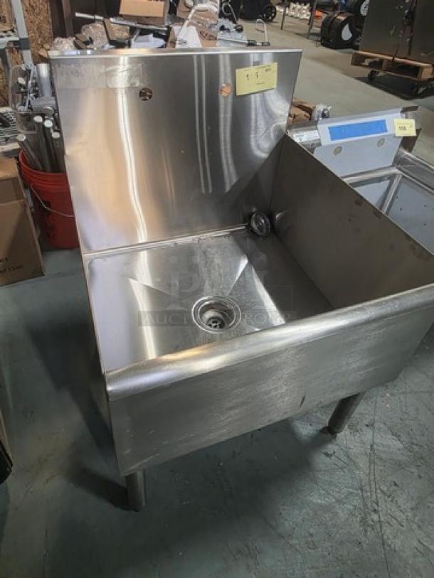 Commercial stainless steel utility sink with high backsplash, central drain, and sturdy legs. Good condition, ideal for industrial use.