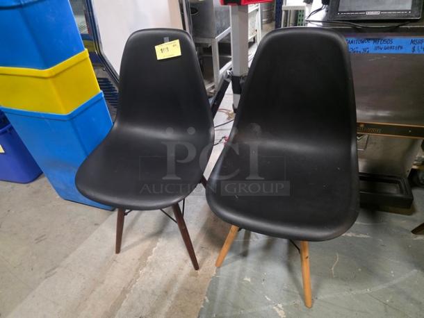 Pair of black armless dining chairs, molded seats, wooden legs, one with a sticker reading "113," used condition.