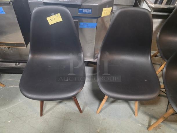 Pair of armless dining chairs with black molded plastic seats and wooden legs. Visibly used condition with price tags.