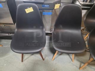 Pair of armless dining chairs with black molded plastic seats and wooden legs. Visibly used condition with price tags.