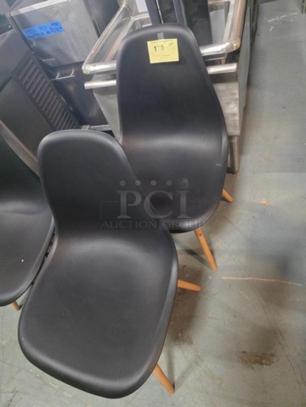 Lot of 2 armless dining chairs, black plastic seats, wooden legs, modern design. Excellent condition. Auction label visible.