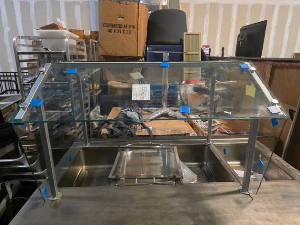 Glass sneeze guard with a stainless steel frame, shown without a steam table, in good condition.