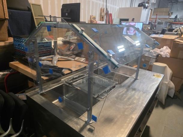 Clear glass sneeze guard with metal supports, displayed on a countertop. Steam table not included. New condition.