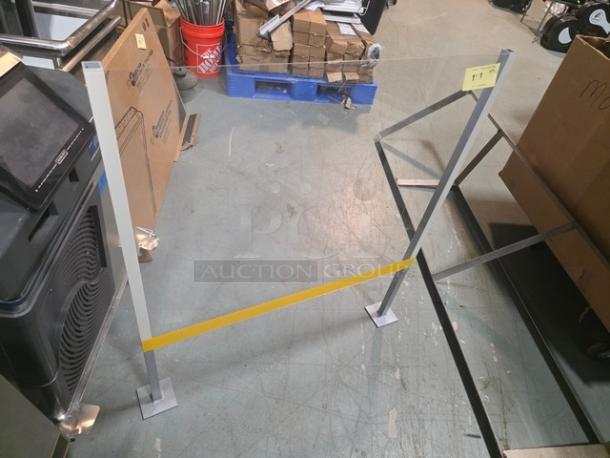 Freestanding sneeze guard with metal frame, clear acrylic panel, and yellow stripe. In good condition, ideal for counters.