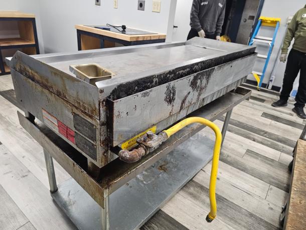 MoTak 60" natural gas griddle in used condition, visible wear and grease; includes gas connection. Stand not included.
